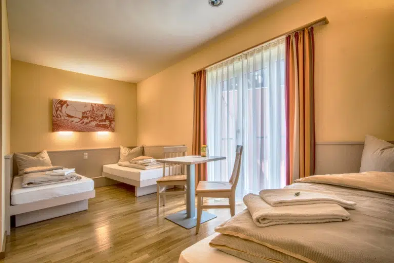 Ihr seht Betten im Familienzimmer im JUFA Hotel Jülich***s mit Tisch. Der Ort für kinderfreundlichen und erlebnisreichen Urlaub für die ganze Familie.