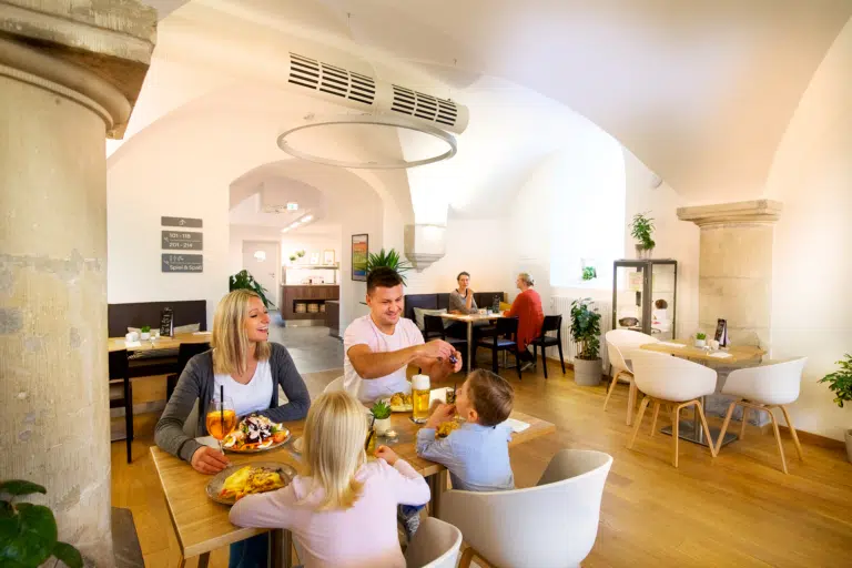 Ihr seht eine Familie beim Essen im Restaurant des JUFA Hotel Festung Rosenberg Kronach. Der Ort für kinderfreundlichen und erlebnisreichen Urlaub für die ganze Familie.