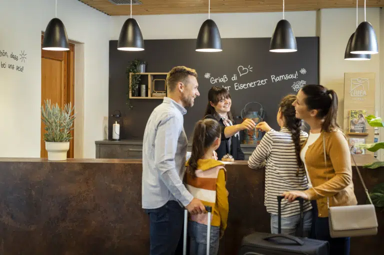 Ihr seht eine Familie bei ihrer Ankunft an der Rezeption. Das JUFA Hotel Eisenerz ist der ideale Ausgangspunkt für Ihren Wander- und Winterurlaub