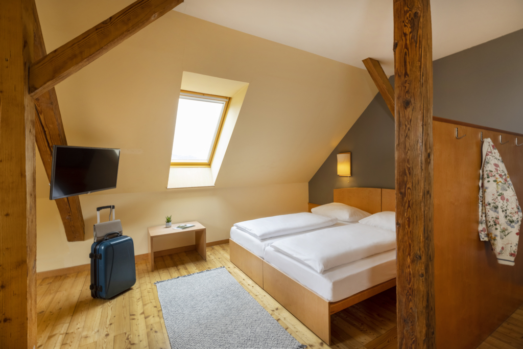 Ihr seht ein Doppelbett. So sind die Doppelzimmer und Einzelzimmer im JUFA Hotel Judenburg ausgestattet. Der Ort für erholsamen Familienurlaub und einen unvergesslichen Winter- und Wanderurlaub.