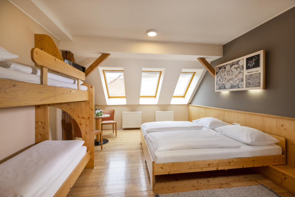 Ihr seht ein Doppelbett und ein Stockbett mit zwei Betten. So sind die Family Friends 4 Zimmer im JUFA Hotel Judenburg ausgestattet. Der Ort für erholsamen Familienurlaub und einen unvergesslichen Winter- und Wanderurlaub.