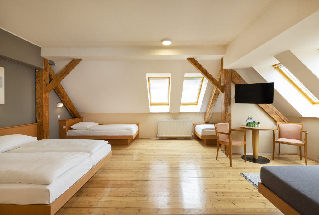 Ihr seht ein Doppelbett und drei Einzelbetten. So sind die Family Friends 5 Zimmer im JUFA Hotel Judenburg ausgestattet. Der Ort für erholsamen Familienurlaub und einen unvergesslichen Winter- und Wanderurlaub.