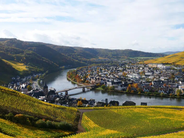 Ihr seht die herbstliche Landschaft mit Moselverlauf in Bernkastel-Kues mit Weinbergen und der Altstadt.