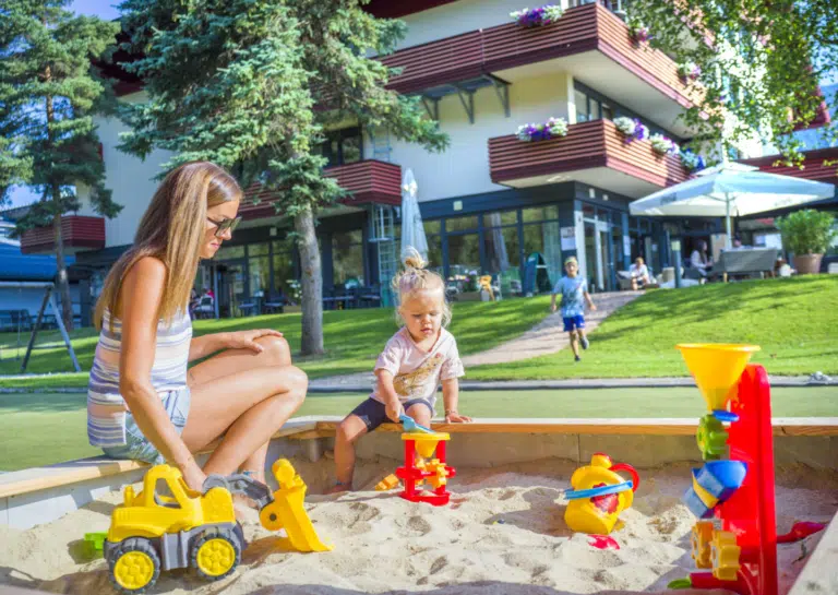 Ihr seht eine Frau in der Sandkiste mit ihrer kleinen Tochter spielen im JUFA Hotel Altenmarkt***.
