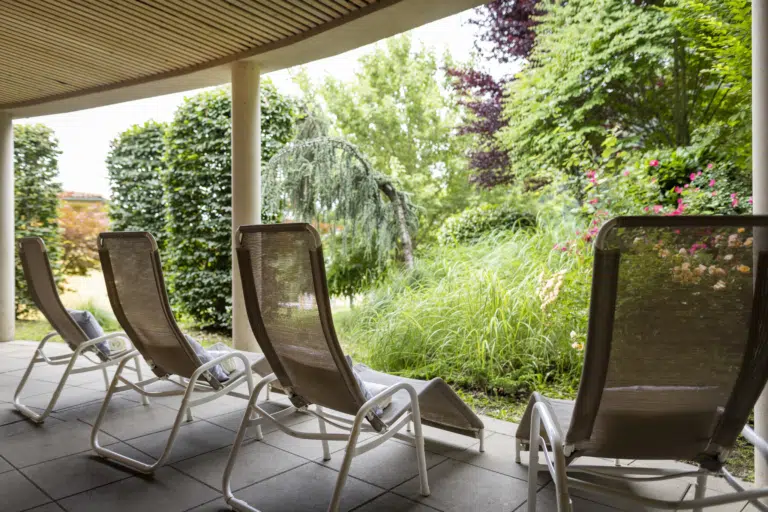 Ihr seht vier komfortable Liegestühle auf der Außenterrasse mit Garten vom Wellness- und Saunabereich im JUFA Hotel Deutschlandsberg*** in der Steiermark.