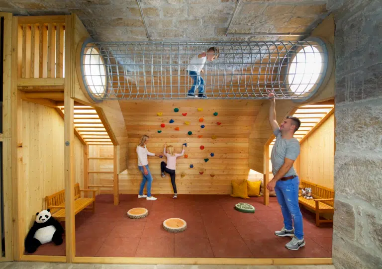 Ihr seht das Spielzimmer mit Kletterröhre und Kindern im JUFA Hotel Festung Rosenberg Kronach. Der Ort für kinderfreundlichen und erlebnisreichen Urlaub für die ganze Familie.
