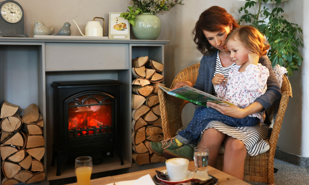 Sie sehen eine Mutter mit ihrer Tochter beim Buch lesen vor einen Kamin im JUFA Hotel Pöllau - Bio-Landerlebnis. Der Ort für erholsamen Familienurlaub und einen unvergesslichen Winter- und Wanderurlaub.