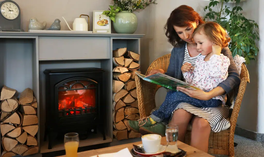 Sie sehen eine Mutter mit ihrer Tochter beim Buch lesen vor einen Kamin im JUFA Hotel Pöllau - Bio-Landerlebnis. Der Ort für erholsamen Familienurlaub und einen unvergesslichen Winter- und Wanderurlaub.
