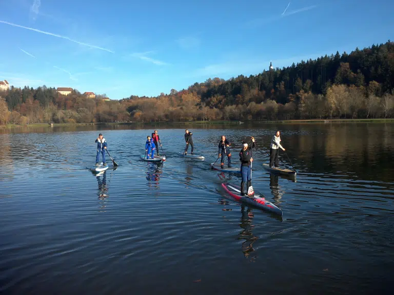 Eine Gruppe beim Stand-Up-Paddling am Sulmsee in der Südsteiermark. JUFA Hotels bietet tollen Sommerurlaub an schönen Seen für die ganze Familie.