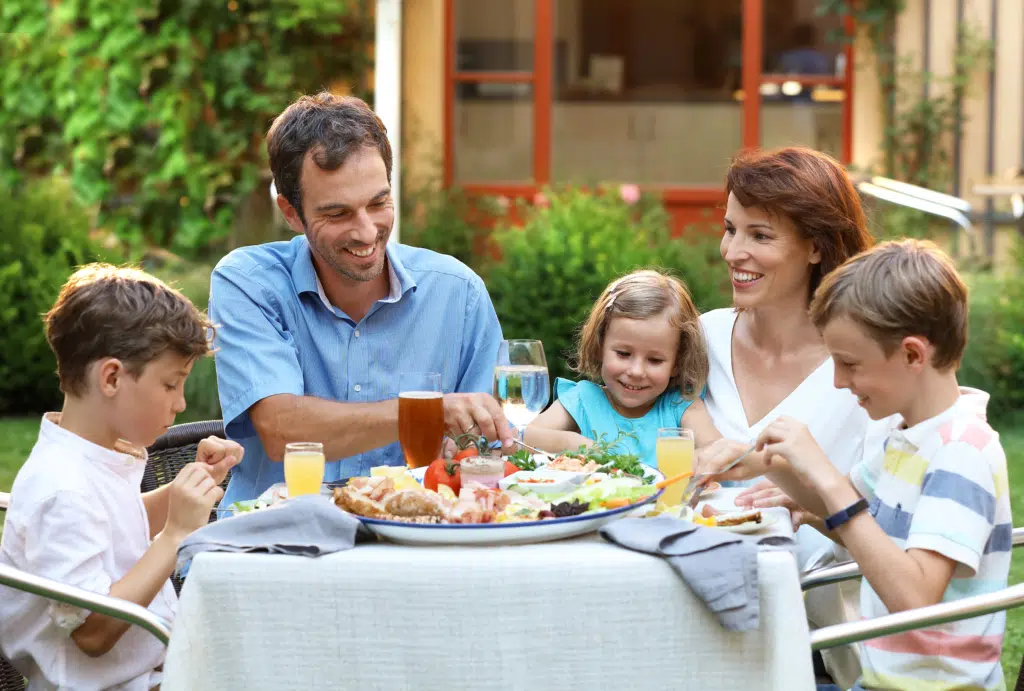 Sie sehen eine Familie bei einer Jause auf der Terrasse des JUFA Hotels Pöllau - Bio-Landerlebnis. Der Ort für erholsamen Familienurlaub und einen unvergesslichen Winter- und Wanderurlaub.