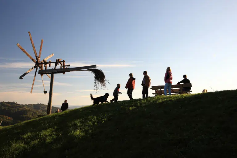 Landschaft mit Klapotetz in Sulmtal-Sausal mit einer Gruppe von Menschen, die die wunderschöne Abendstimmung genießt. JUFA Hotels bietet euch den Ort für erlebnisreichen Natururlaub für die ganze Familie.