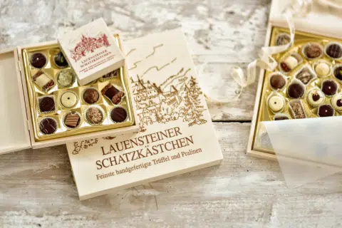 Ihr seht zwei Pralinenschachteln mit Schokopralinen von Lauenstein Confiserie, die das JUFA Hotel Kronach – Festung Rosenberg beliefert. JUFA Hotels bietet kinderfreundlichen und erlebnisreichen Urlaub für die ganze Familie.