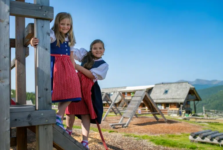 Ihr seht Mädchen im Dirndl am Spielplatz bei der Hiaslhütte in den Nockbergen.