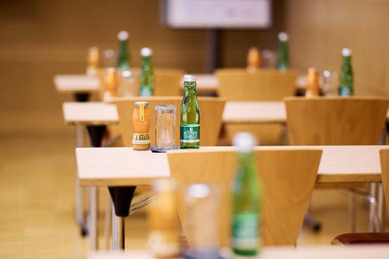 Ihr seht einen Seminarraum mit Seminartischen mit Römerqulle und Rauchsaft im JUFA Hotel Wien City****. Der Ort für eure erfolgreichen Seminare, Workshops und Tagungen.