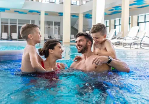 Ihr seht eine Familie mit Kindern beim Baden und Entspannen im Innenbereich einer Therme in der Nähe von JUFA Hotels.