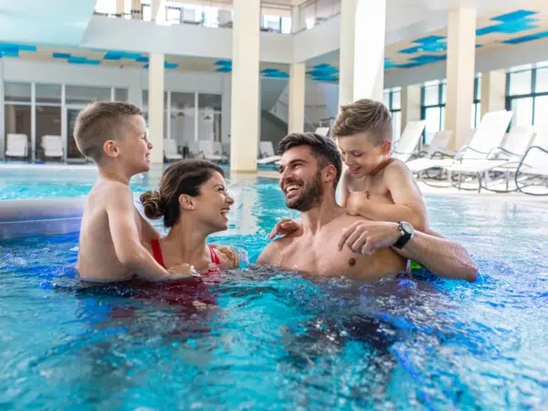 Ihr seht eine Familie mit Kindern beim Baden und Entspannen im Innenbereich einer Therme in der Nähe von JUFA Hotels.