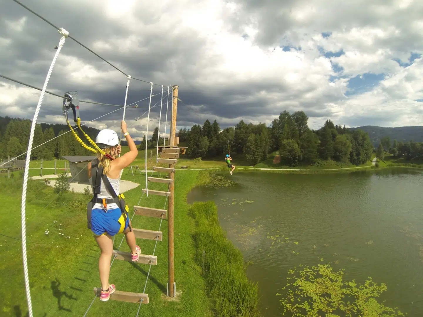 Ihr seht ein Mädchen auf einer Hängebrücke im Outdoorparc Lungau im Sommer. JUFA Hotels bietet erlebnisreiche Feriencamps in den Bereichen Sport, Gesundheit, Bildung und Sprachen.