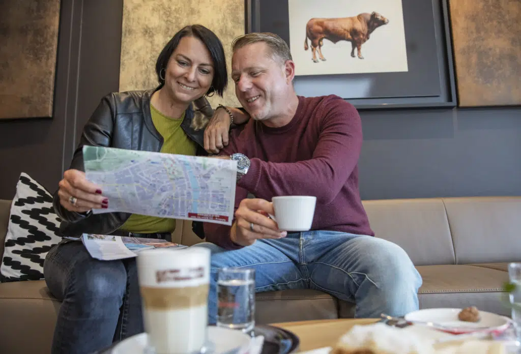Ihr seht ein Paar mit Kaffee in der Lobby im JUFA Hotel Salzburg City. Der Ort für erholsamen Familienurlaub und einen unvergesslichen Winter- und Wanderurlaub.