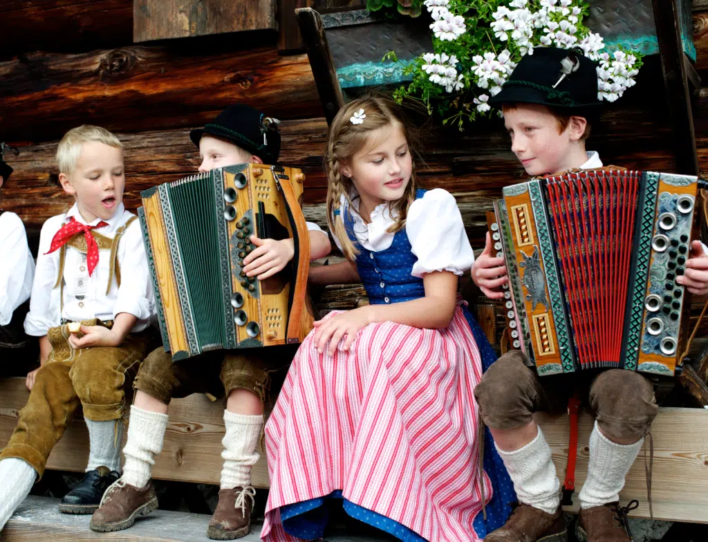 Ihr seht Kinder beim Bauernherbst auf einer Bank sitzen und musizieren