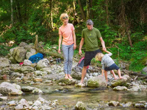 Ihr seht eine Familie wie sie sich abkühlt am Bach im Salzkammergut. JUFA Hotels bietet erholsamen Familienurlaub und einen unvergesslichen Winter- und Wanderurlaub.