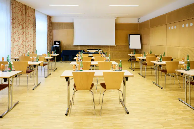 Ihr seht den Seminarraum Symphonia im JUFA Hotel Wien City****. Der Raum ist gefüllt mit Sesseln und Tischen. Auf den Tischen befinden sich Blöcke, Stifte und Getränke. Im Hintergrund ist ein Beamer, eine Leinwand und ein Flipchart. Der Ort für eure erfolgreichen Seminare, Workshops und Tagungen.
