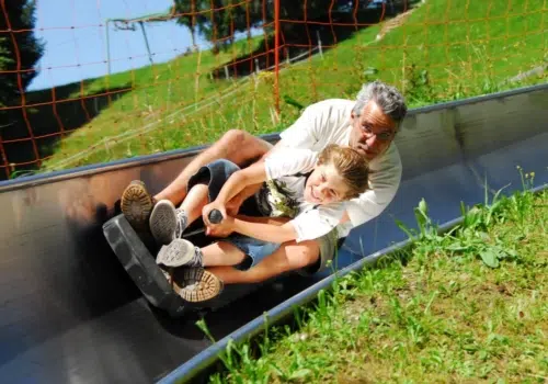 Ihr seht einen Vater mit Kind auf der Sommerrodelbahn Laterns-Gapfohl. Die JUFA Hotels bieten erholsamen Urlaub für die ganze Familie.
