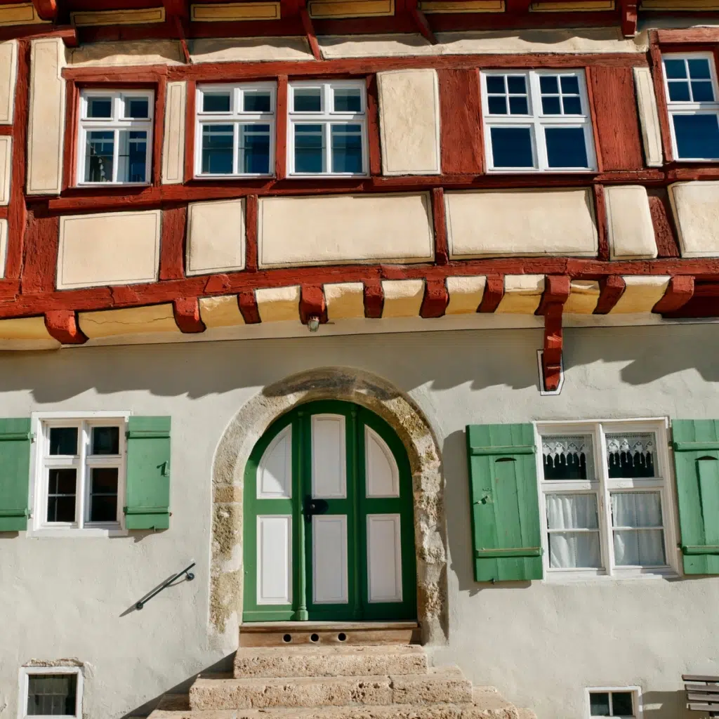 Historisches Fachwerkhaus in Nördlingen mit rotem Gebälk, grünen Fensterläden und Rundbogentür – Kulisse und Inspiration für den Anime Attack on Titan nahe dem JUFA Hotel Nördlingen.