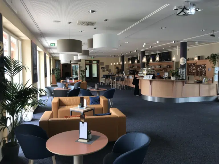 Offener Rezeptions- und Lobbybereich im JUFA Hotel Nördlingen mit Empfangstresen, Bar, modernen Sitzgruppen und großen Fenstern.