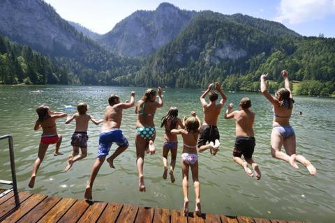 Teens springen vom Steg in den Gleinkersee in Oberösterreich im Sommer. JUFA Hotels bietet tollen Sommerurlaub an schönen Seen für die ganze Familie.