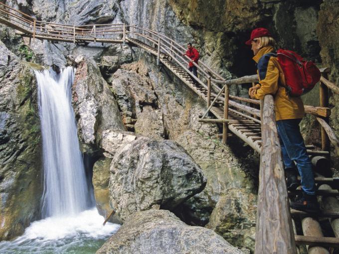 Besucher in der Bärenschützklamm auf einem Holzleiterweg neben einem Wasserfall in der Nähe von JUFA Hotels. Der Ort für erholsamen Familienurlaub und einen unvergesslichen Winter- und Wanderurlaub.