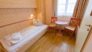 Bett im Einzelzimmer im JUFA Hotel Gitschtal Landerlebnis mit Tisch. Der Ort für kinderfreundlichen und erlebnisreichen Urlaub für die ganze Familie.