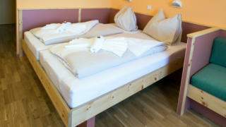 Doppelbett im Doppelzimmer im JUFA Hotel Planneralm Alpin-Resort mit Bettleuchten. Der Ort für erholsamen Familienurlaub und einen unvergesslichen Winter- und Wanderurlaub.