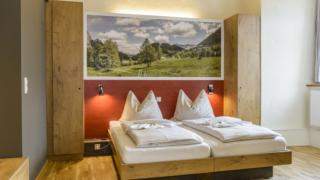Doppelbett im Doppelzimmer im JUFA Hotel Pyhrn-Priel mit Wandbild. Der Ort für erfolgreiche und kreative Seminare in abwechslungsreichen Regionen.
