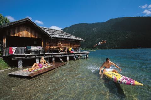 Familie vergnügt sich am Weissensee in Kärnten mit Surfbrett im Sommer. JUFA Hotels bietet Ihnen den Ort für erlebnisreichen Natururlaub für die ganze Familie.