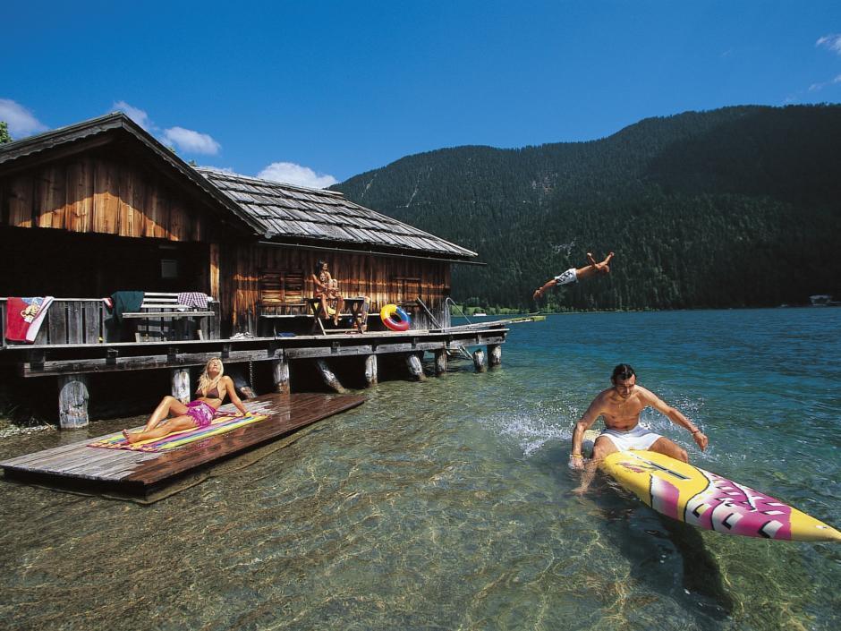 Familie vergnügt sich am Weissensee in Kärnten mit Surfbrett im Sommer. JUFA Hotels bietet Ihnen den Ort für erlebnisreichen Natururlaub für die ganze Familie.