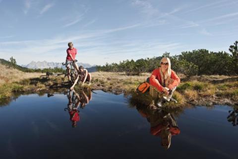 Sportler machen Pause beim Wandern und Mountainbiken an einem Bergsee in Altenmarkt-Zauchensee in der Nähe von JUFA Hotels. Der Ort für erholsamen Familienurlaub und einen unvergesslichen Winter- und Wanderurlaub.