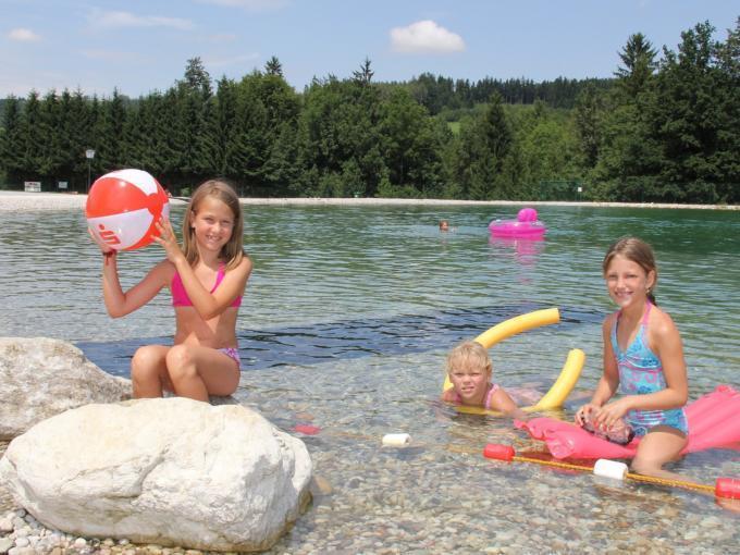 Kinder planschen am Ufer des Badesees St. Konrad im Salzkammergut an einem heißen Sommertag. JUFA Hotels bietet kinderfreundlichen und erlebnisreichen Urlaub für die ganze Familie.