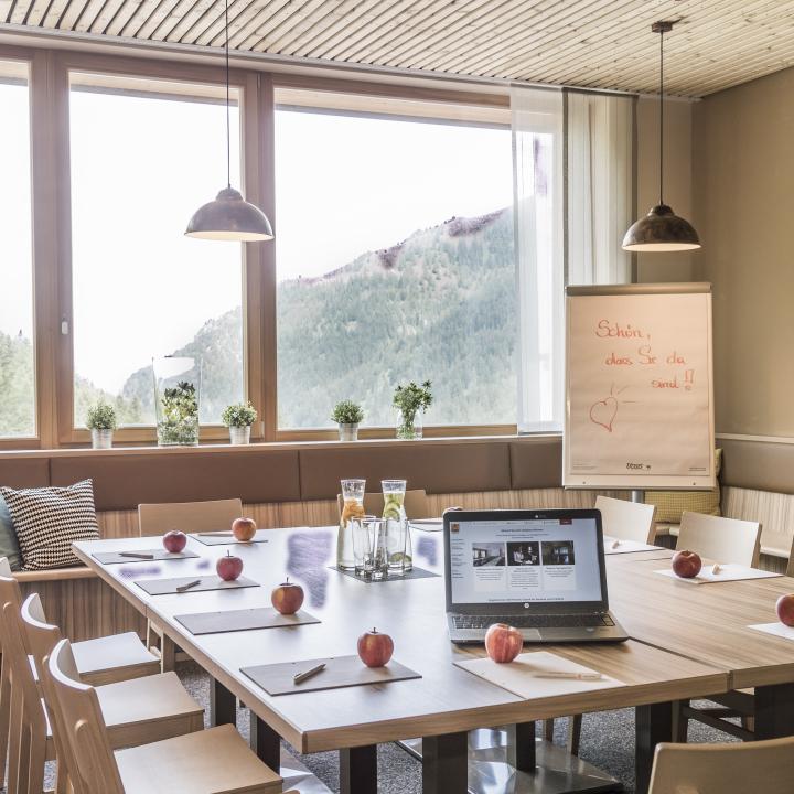 Besprechungstischmit Laptop und Äpfeln im Restaurantbereicht im JUFA Hotel Malbun Alpin-Resort. Der Ort für erholsamen Familienurlaub und einen unvergesslichen Winter- und Wanderurlaub.