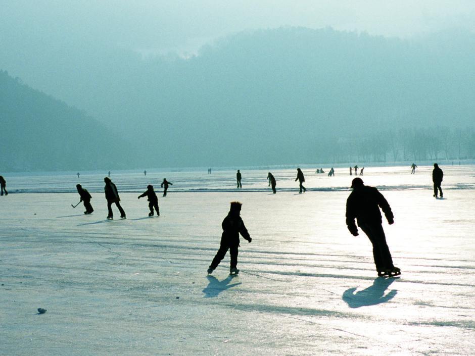Familien beim Eislaufen auf dem zugefrorenen Leopoldsteiner See in der Steiermark. JUFA Hotels bietet erholsamen Familienurlaub und einen unvergesslichen Winterurlaub.