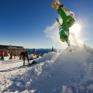 Snowboarder bei gewagtem Stunt auf der Gemeindealpe Mitterbach am Erlaufsee mit Skifahrern im Hintergrund. JUFA Hotels bietet erholsamen Familienurlaub und einen unvergesslichen Winterurlaub.