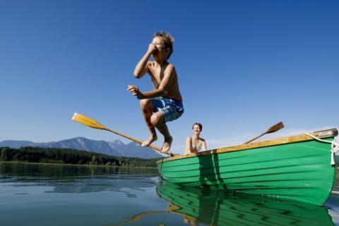 Junge springt vom Ruderboot in den Turnersee im Sommer. JUFA Hotels bietet tollen Sommerurlaub an schönen Seen für die ganze Familie.