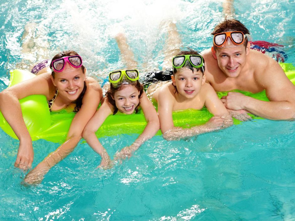 Sie sehen eine Familie mit Schwimmbrillen liegend auf einer grünen Luftmatratze im Pool. JUFA Hotels bietet erholsamen Thermen- und Badespass für die ganze Familie.