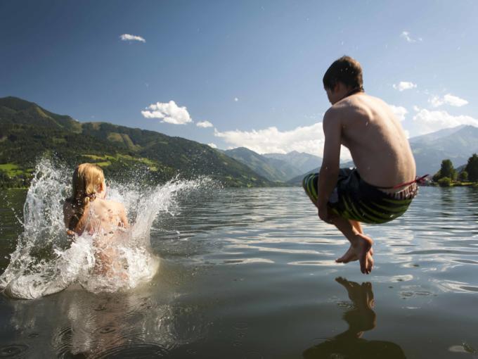 Zwei Kinder springen mit Arschbombe in einen See. JUFA Hotels bietet tollen Sommerurlaub an schönen Seen für die ganze Familie.