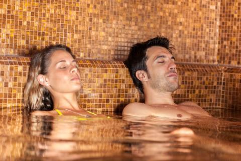 Sie sehen ein Paar liegend und erholend im Thermalbecken. JUFA Hotels bietet erholsamen Thermen- und Badespass für die ganze Familie.