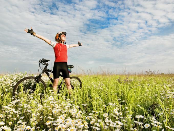 Ein Mann mit einem Mountainbike steht mitten in einer Blumenwiese und genießt während einer Pause die Natur. JUFA Hotels bietet Ihnen den Ort für erlebnisreichen Natururlaub für die ganze Familie.