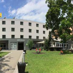 Aussenansicht mit Eigangsbereich und Garten vom JUFA Hotel Graz City. Der Ort für erlebnisreichen Städtetrip für die ganze Familie und der ideale Platz für Ihr Seminar.