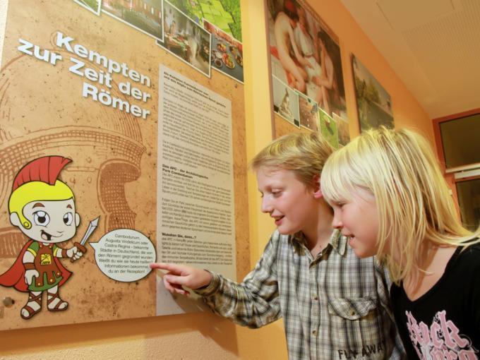 Zwei Kinder informieren sich über die Römerzeit in Kempten via Infotafeln im JUFA Kempten Familien-Resort. Der Ort für kinderfreundlichen und erlebnisreichen Urlaub für die ganze Familie.