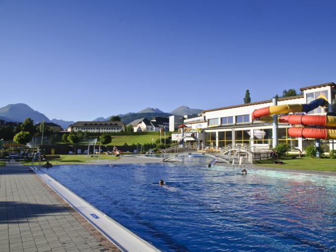 Badegäste beim Schwimmen im Außenbecken der Badeinsel Tamsweg mit Wasserrutsche im Sommer. JUFA Hotels bieten erholsamen Familienurlaub und einen unvergesslichen Winter- und Wanderurlaub.