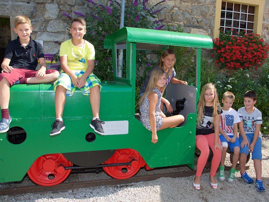 Kinder sitzen im Sommer auf einer grünen Lokomotive vorm Schaubergwerk in der Nähe vom JUFA Hotel Knappenberg. Der Ort für erlebnisreiche und kreative Schulprojektwochen in abwechslungsreichen Regionen.