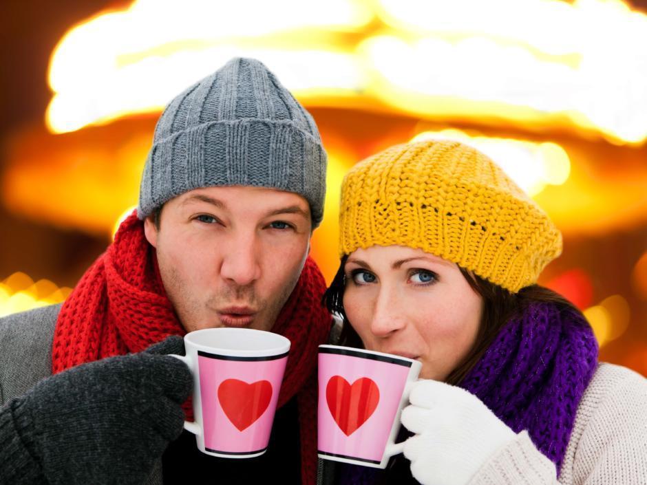 Ein Paar mit Hauben trinkt aus Herztassen Gülühwein auf einem Adventmarkt. JUFA Hotels bietet erholsamen Familienurlaub und einen unvergesslichen Winterurlaub.